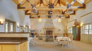 A spacious dining area with wooden tables and chairs, a stone fireplace, and exposed wooden beams. - Riverfront mountain townhouse with pool & hot tub, patio, & easy ski access (Government Camp)