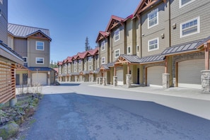 A row of multi-story buildings with attached garages, a paved driveway, and stone pillars. - Riverfront mountain townhouse with pool & hot tub, patio, & easy ski access (Government Camp)