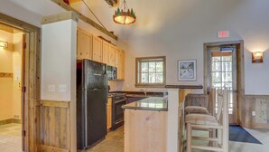 A kitchen with wooden cabinets, a black refrigerator, a stove, and a window. - Riverfront mountain townhouse with pool & hot tub, patio, & easy ski access (Government Camp)