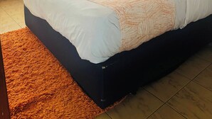 Uma cama com roupa de cama branca e laranja, uma cabeceira preta e um tapete castanho.