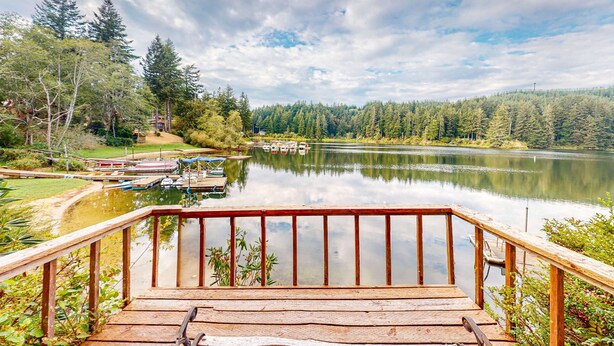 Eine Holzterrasse führt zu einem ruhigen See mit angestoßenen Booten, umgeben von dichtem Wald.