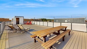 Een houten terras met een picknicktafel en stoelen, een klein gebouw en een uitzicht op de lucht en het verre landschap.