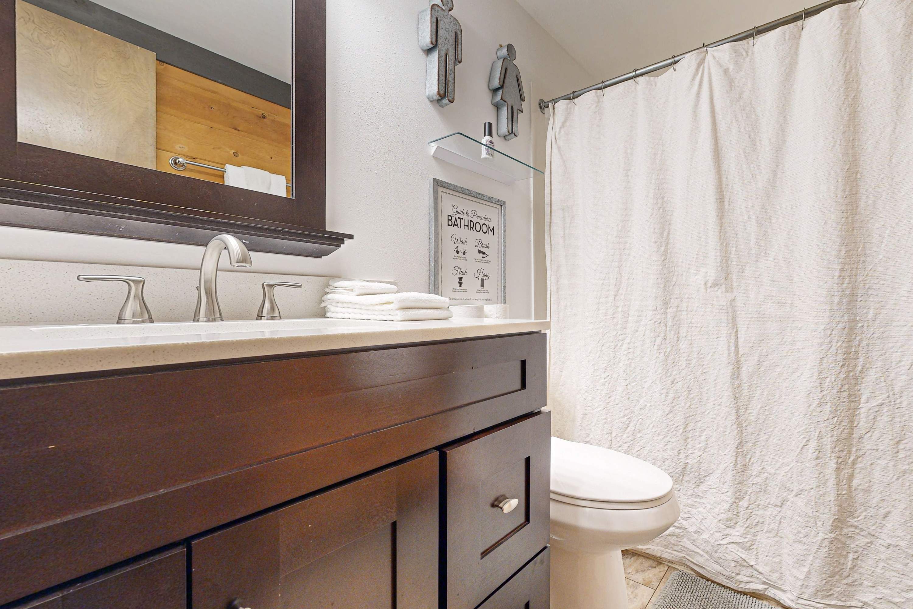 A bathroom with a wooden vanity, a white toilet, a glass shower enclosure, and a mirror with a towel rack.