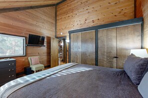 Een slaapkamer met een bed, een dressoir, een televisie, een stoel en een kledingkast.
