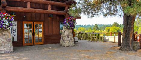 A log cabin-style building with a stone foundation, wooden doors, and a stone pillar with a hanging flower basket.