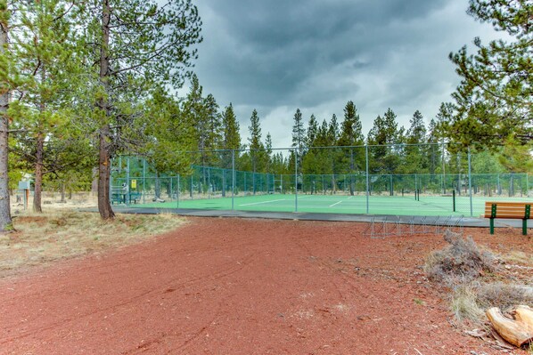 A tennis court with a green fence, a bench, and trees in the background. - in Sunriver with SHARC amenities, washer&dryer, & dog-friendly (Sunriver)