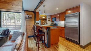 A kitchen with wooden cabinets, a stainless steel refrigerator, and a bar area with stools. - in Sunriver with SHARC amenities, washer&dryer, & dog-friendly (Sunriver)