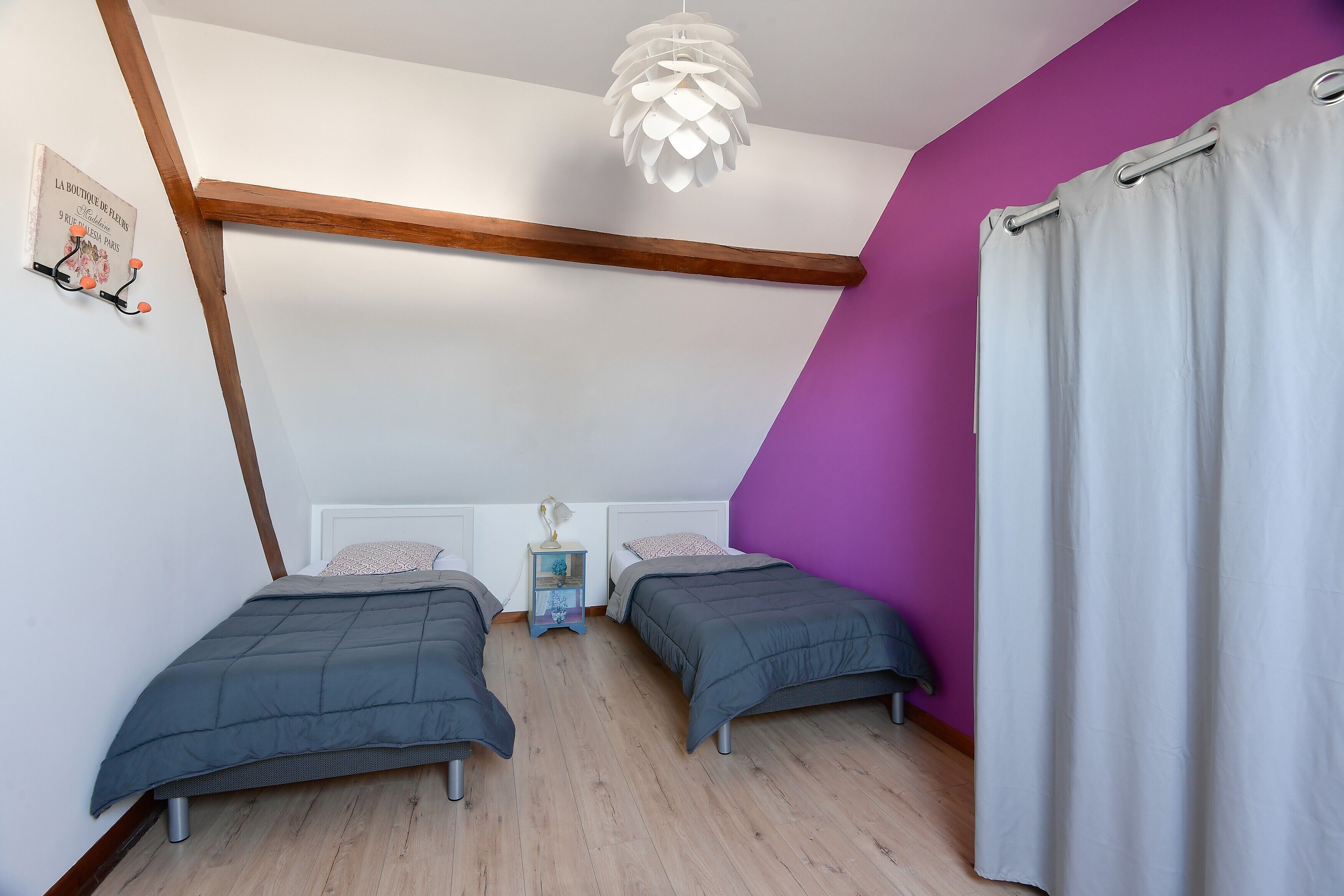 A bedroom with two beds, a wooden beam ceiling, a hanging light fixture, a nightstand, and a purple wall.