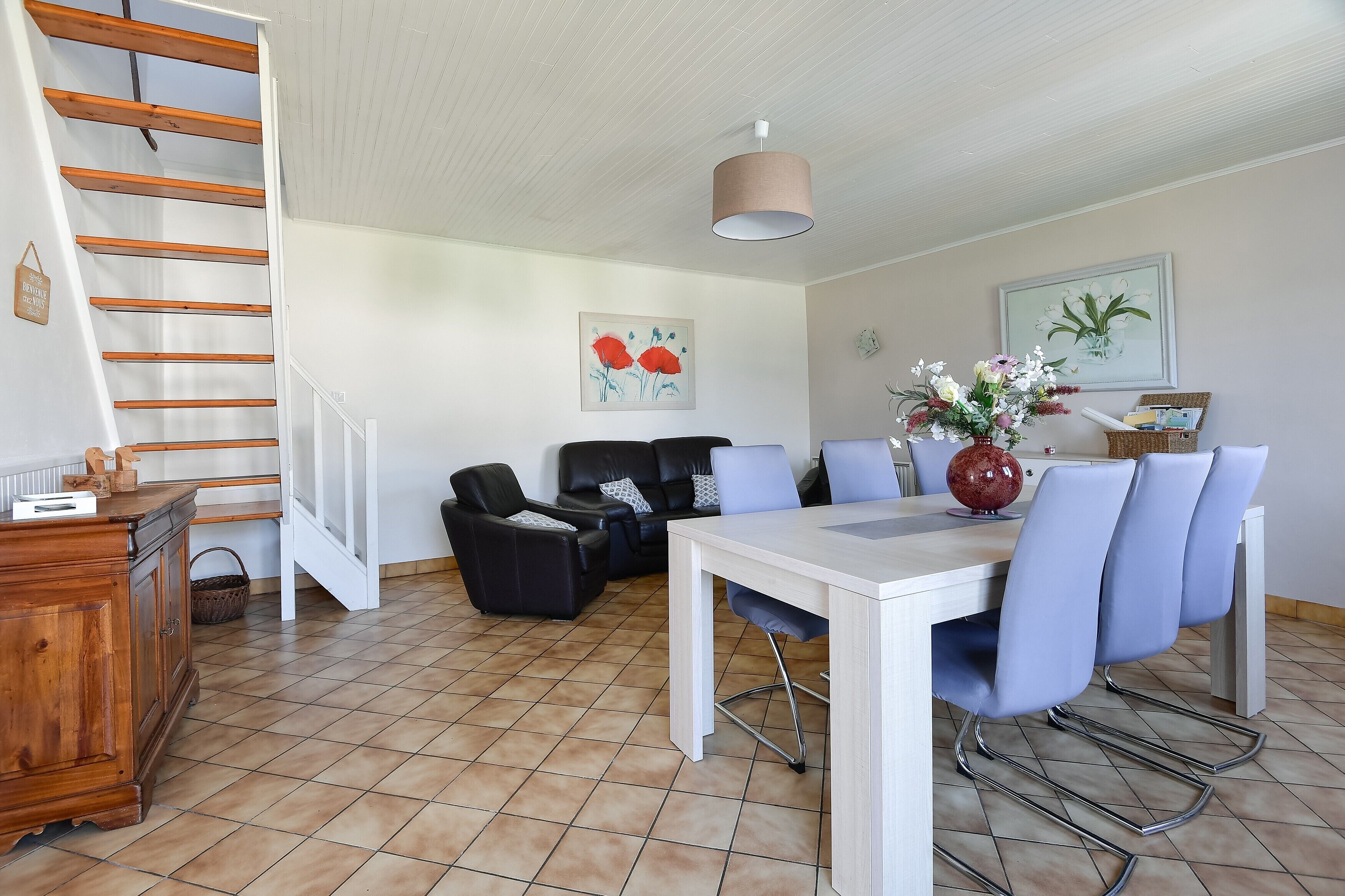 A spacious living area with a dining table, chairs, a sofa, a staircase, and a ceiling light.