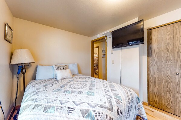 A bedroom with a patterned bedspread, a bedside lamp, a wardrobe, and a door leading to another room. - Classic lakefront home with private hot tub, fireplace & washer&dryer (Joseph)
