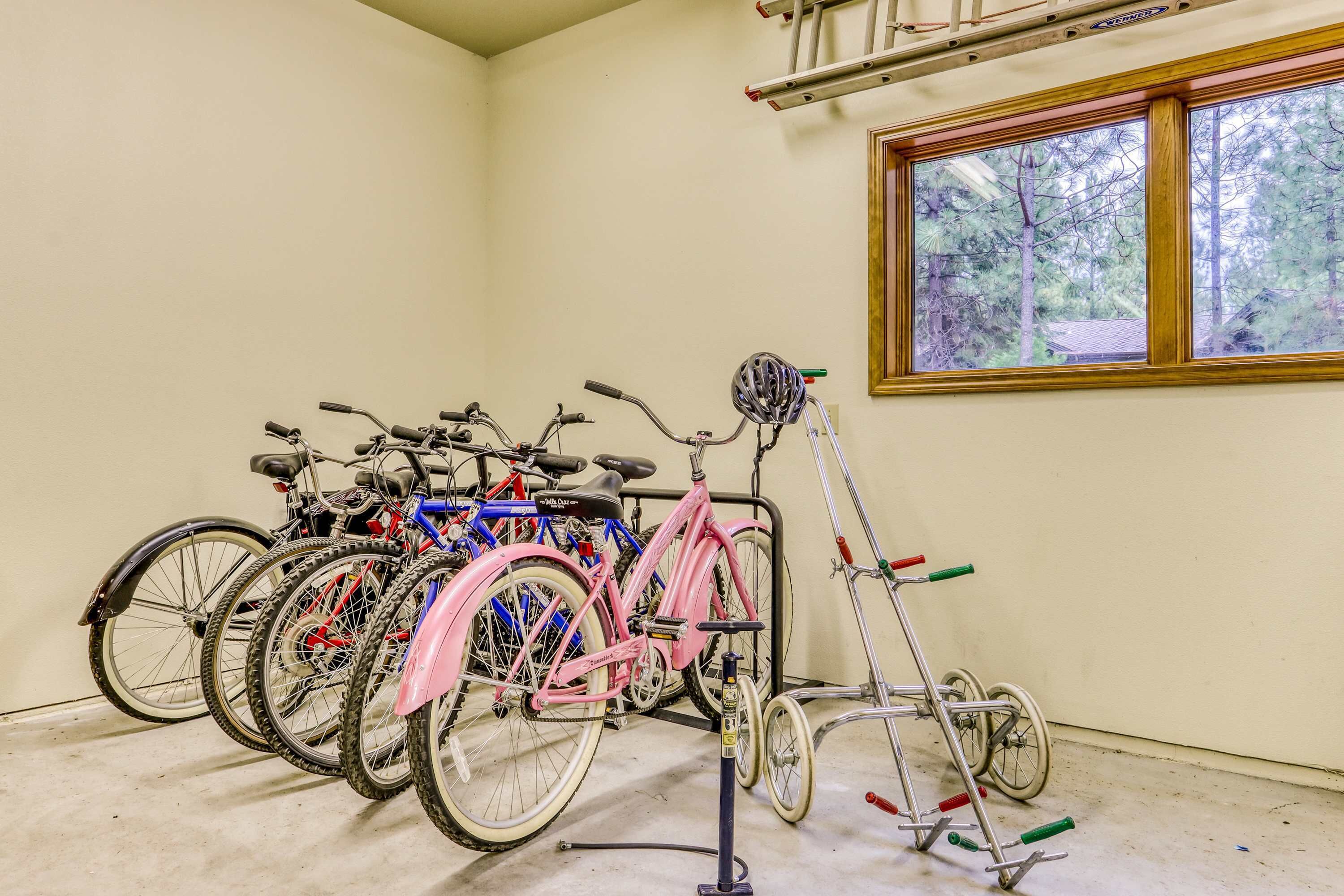 A room with bicycles parked against the wall, a window with a view of trees, and a ceiling with exposed pipes.