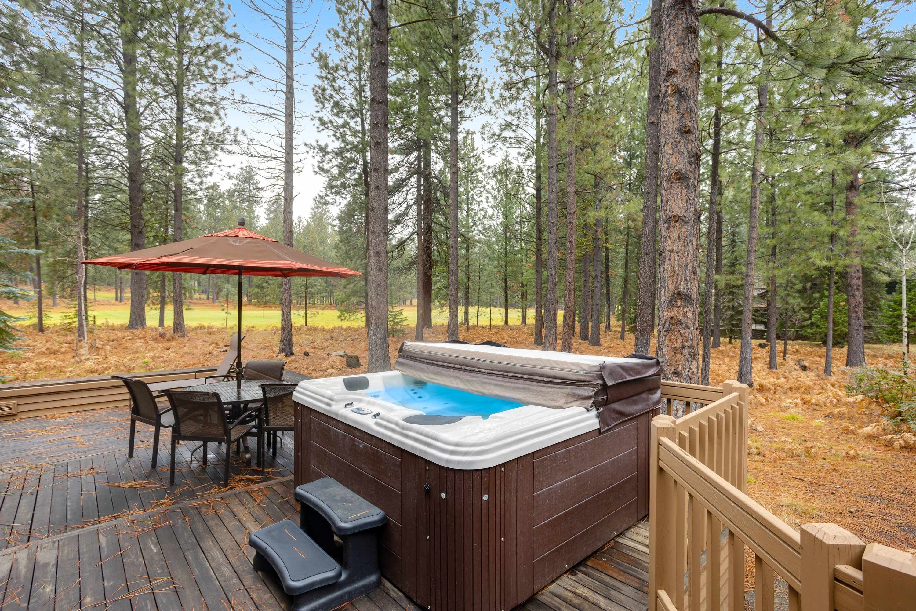 A hot tub on a wooden deck surrounded by tall pine trees.