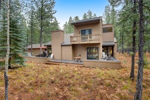 A modern two-story cabin with a deck, surrounded by a forest.
