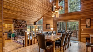 A wooden interior with a dining area, stone fireplace, and large windows. - Forested getaway with kitchen, stone fireplace, pool, & private hot tub (Black Butte Ranch)
