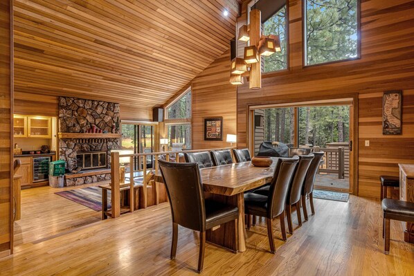 A wooden interior with a dining area, stone fireplace, and large windows.