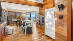 A modern kitchen with wooden cabinetry, a dining area with a table and chairs, and a view through large windows. - Secluded beachfront home with Pacific Ocean views, fireplace, game room, grill (Arch Cape)