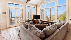 A spacious living room with a large sectional sofa, a flat-screen TV, and a bookshelf. - Secluded beachfront home with Pacific Ocean views, fireplace, game room, grill (Arch Cape)