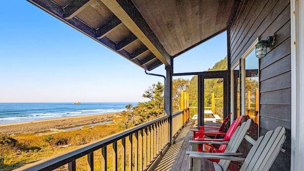 A wooden deck with chairs overlooking a beach and ocean. - Secluded beachfront home with Pacific Ocean views, fireplace, game room, grill (Arch Cape)