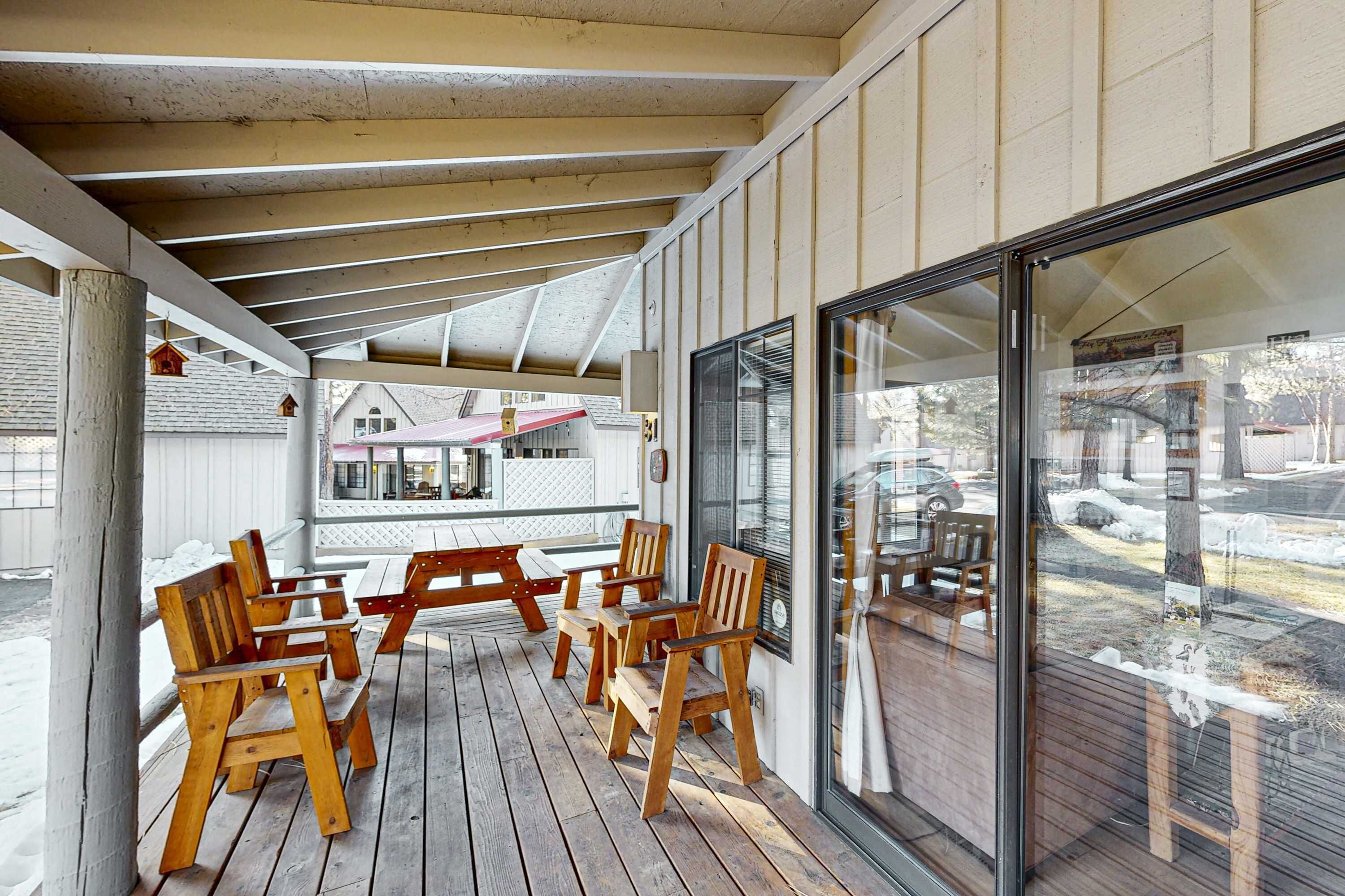 A covered outdoor seating area with wooden benches and tables, a glass door, and a view of the street.
