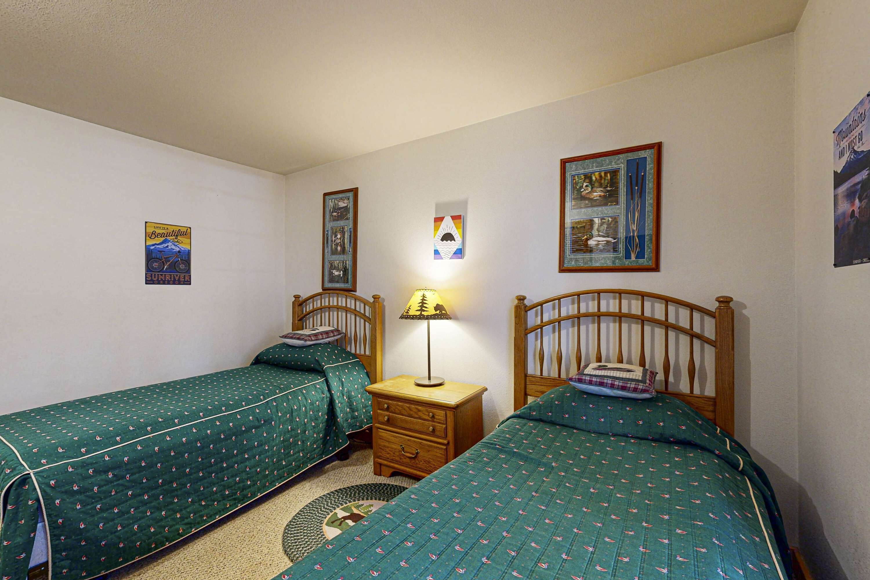 Un dormitorio con dos camas individuales, una mesita de noche con lámpara y cuadros en las paredes.