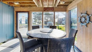 Ein überdachter Außenbereich mit einem runden Tisch und Korbstühlen, einer Holzzieldecke und Blick ins Freie.