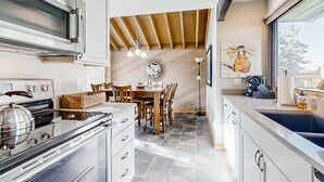A modern kitchen with a built-in oven, a dining area with wooden chairs, and a large window providing a view. - Updated home golf course view, pool, & tennis - wood fireplace, grill, and deck (Sunriver)