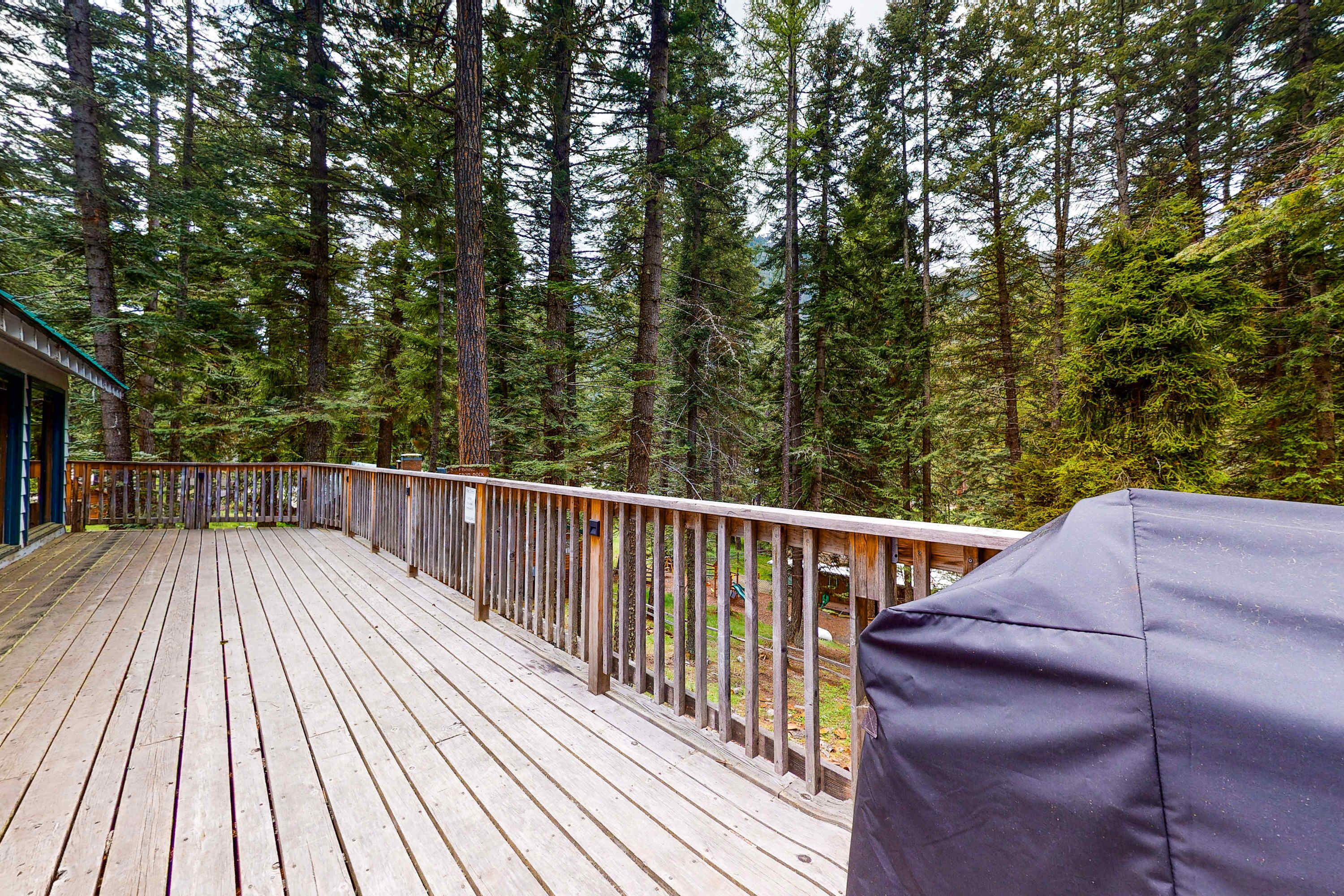 A wooden deck with a railing, surrounded by tall trees.