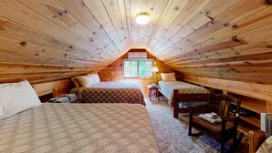Ein gemütliches Schlafzimmer im Dachgeschoss mit Holzwänden und geneigten Decken, zwei Betten, einem kleinen Tisch und einem Stuhl.