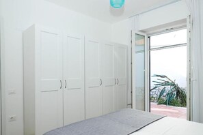 Un dormitorio con cama, armario blanco y puerta corrediza de vidrio a un balcón.