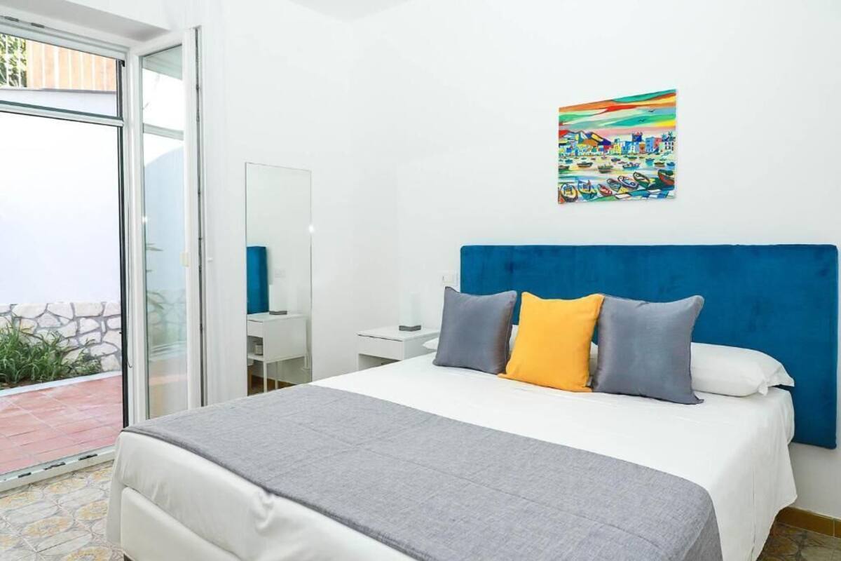 Un dormitorio con una cama, cabecera azul, mesita de noche, espejo y una obra de arte colorida en la pared.