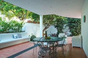An outdoor patio with a round table and chairs, a white sofa with cushions, and potted plants. - Villa Trani - close to the beach (Ischia)