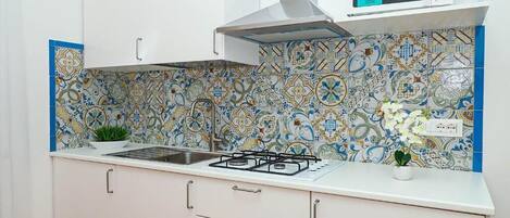 Una cocina con estufa a gas, armarios blancos, microondas y un salpicadero decorativo.