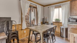 A dining area with a wooden table and chairs, a kitchen with a microwave, and a window with curtains. - Recently updated in 2024-Large, dog-friendly home with covered deck (Government Camp)