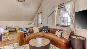 A loft-style bedroom with a sloped ceiling, a large window with curtains, a bed, a bedside table, and a nightstand. - Recently updated in 2024-Large, dog-friendly home with covered deck (Government Camp)