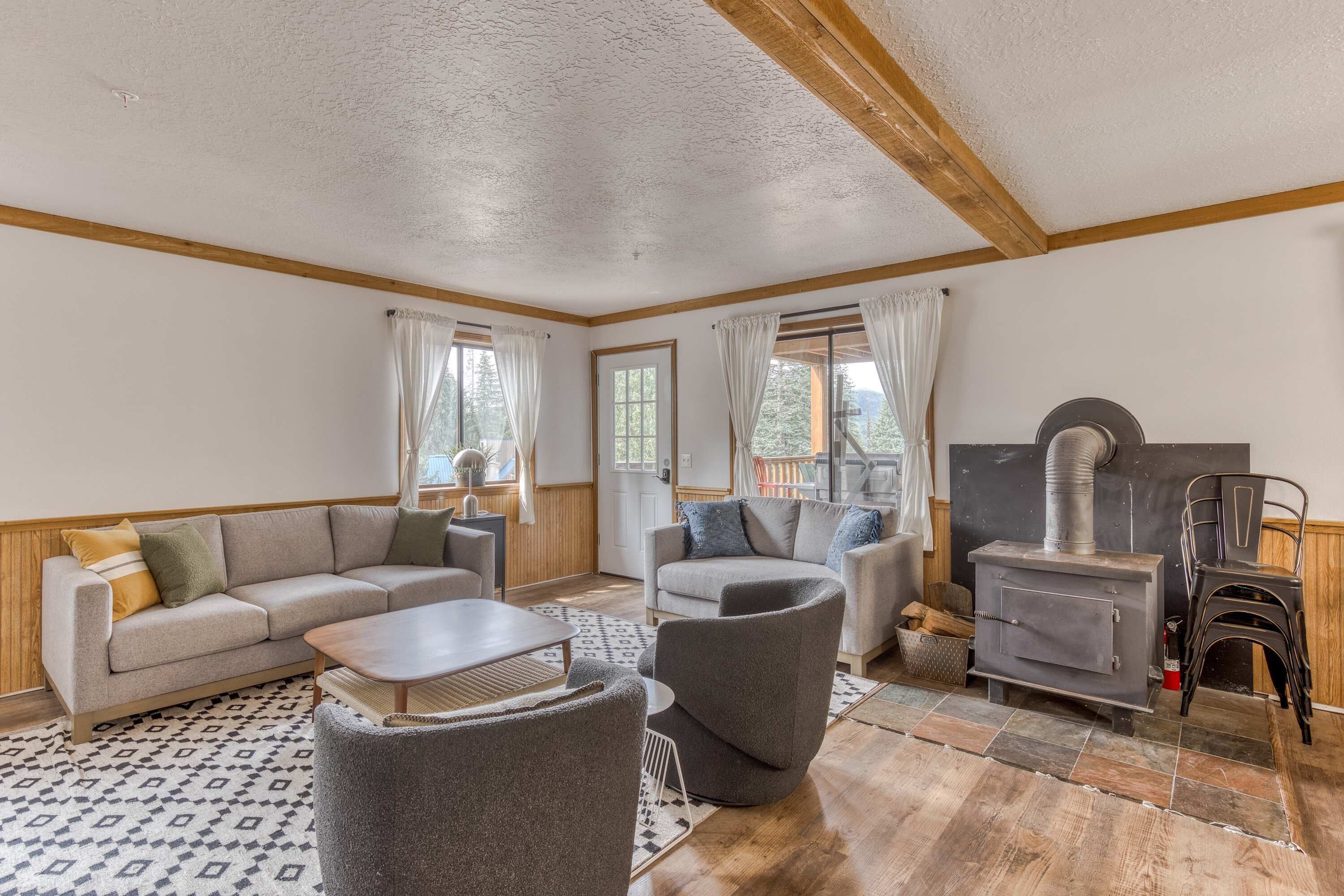 A cozy living room with a sofa, armchairs, a table, a fireplace, and a view of the outdoors.