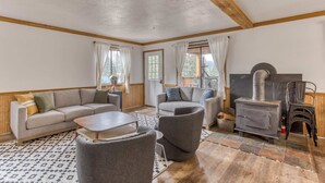 A cozy living room with a sofa, armchairs, a table, a fireplace, and a view of the outdoors. - Recently updated in 2024-Large, dog-friendly home with covered deck (Government Camp)