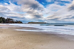 A beach with a lighthouse, ocean waves, and a forested cliff. - Dog-Friendly Home with Wood-Burning Fireplace and Ocean Views - Near the beach (Coos Bay)