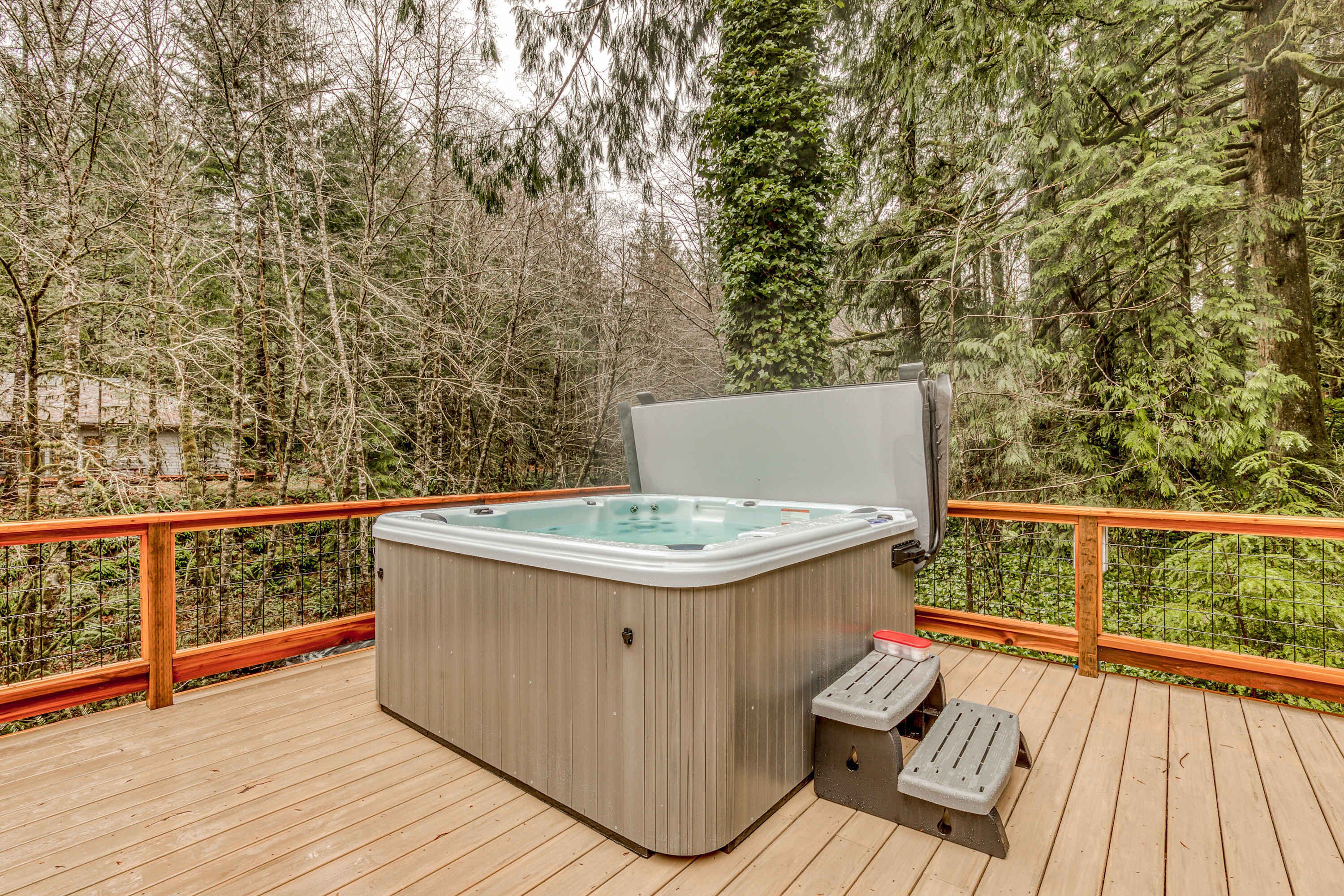 Een hottub op een houten terras met een leuning, omringd door bomen.