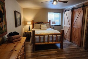 Un dormitorio con cama de madera, ventilador de techo, ventana y puerta corredera estilo granero.