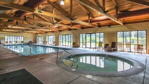 An indoor swimming pool with a wooden ceiling, large windows, and lounge chairs.