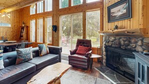 A log cabin interior with a fireplace, leather sofa, dining area, and large windows.