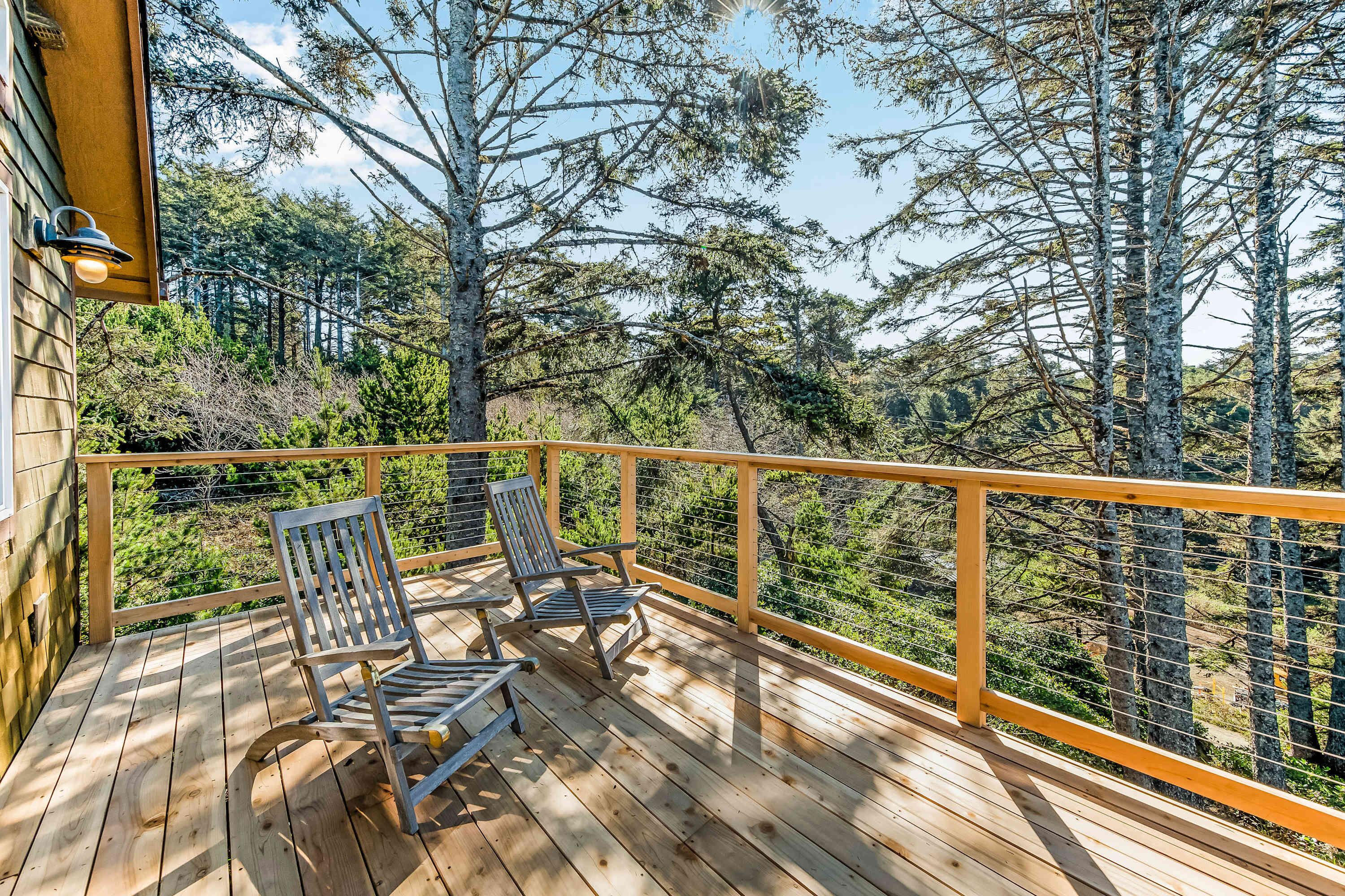 A wooden deck with two chairs and a railing overlooking a forest.
