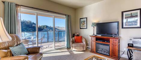 A living room with a sofa, armchair, TV, fireplace, and a view of the ocean.