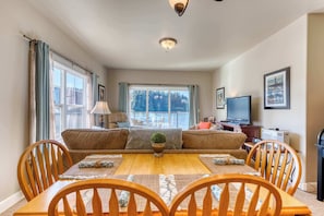 A dining area with a wooden table, chairs, a sofa, and a television in the background.