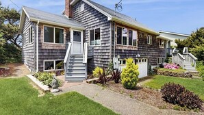 Een twee verdiepingen tellend huis met een veranda, schoorsteen en een kleine tuin met verschillende planten.