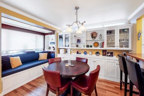 A dining area with a round table, red chairs, a built-in bench with cushions, and a white cabinet with glass doors.