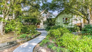 A pathway leading to a house surrounded by lush greenery and trees.