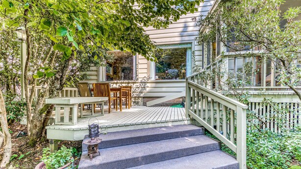 A wooden staircase leading to a porch with a table and chairs, surrounded by greenery.