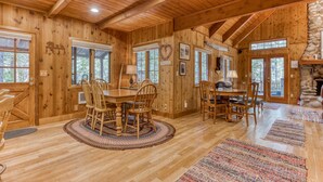 A wooden cabin interior with a dining area, a fireplace, and a stone wall. - Historic Waterfront Cabin with Hot Tub & Salmon River Access - Dog-Friendly (Welches)