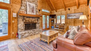 A log cabin interior with a stone fireplace, wooden walls, a leather couch, and a dining area. - Historic Waterfront Cabin with Hot Tub & Salmon River Access - Dog-Friendly (Welches)